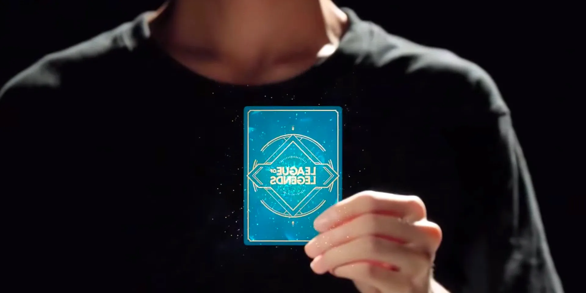 A person in a black shirt holding a blue card with the League of Legends logo on it. Image