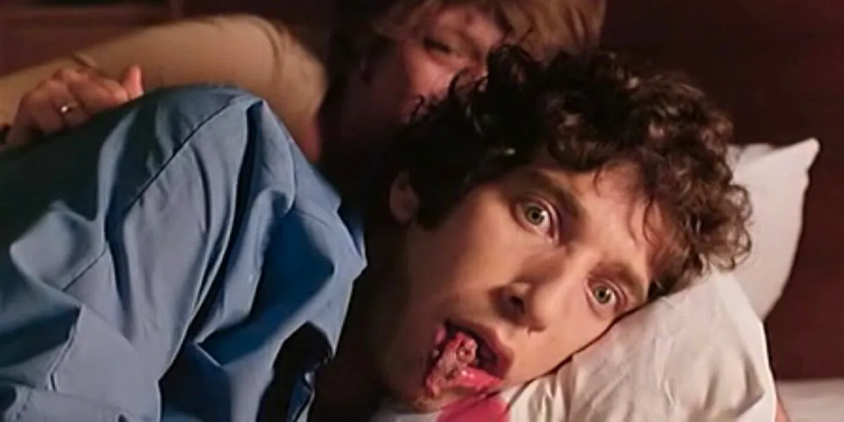 A still from Shivers featuring a man laying on a pillow as a parasite squirms out of his mouth Image