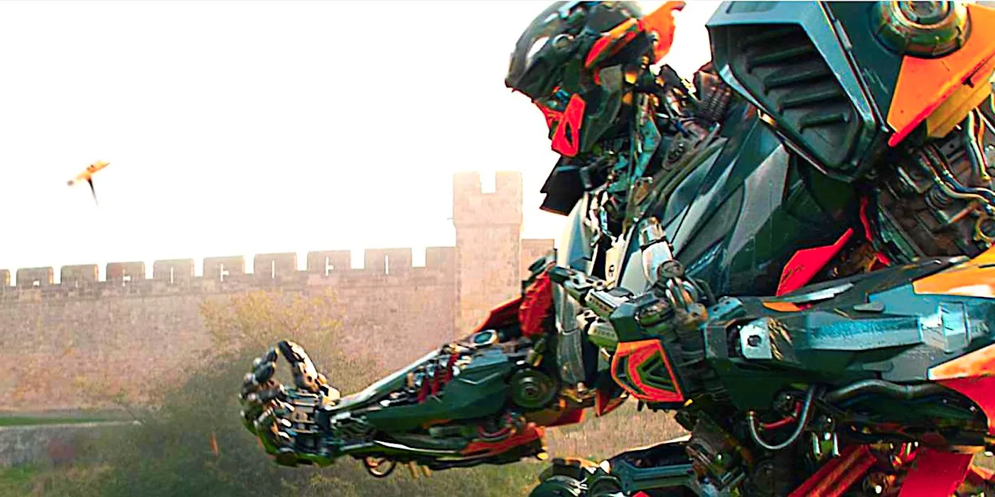 A Transformer stoops down with its hand out beside a castle in Transformers The Last Knight 2017 Image