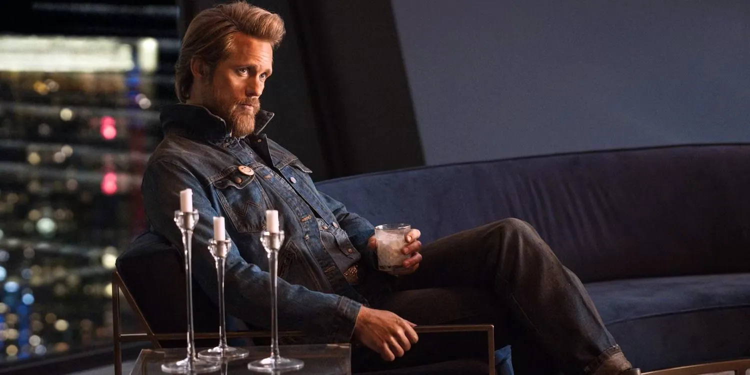 Alexander Skarsgard as Randall Flagg sitting with a drink in hand in The Stand Image