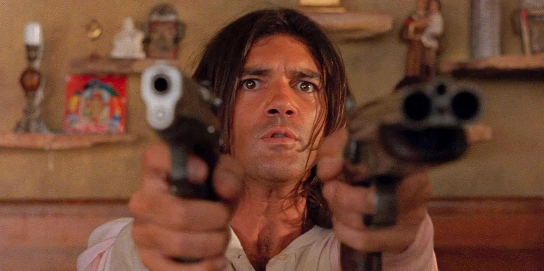 Antonio Banderas points two guns out in front of him.  Image