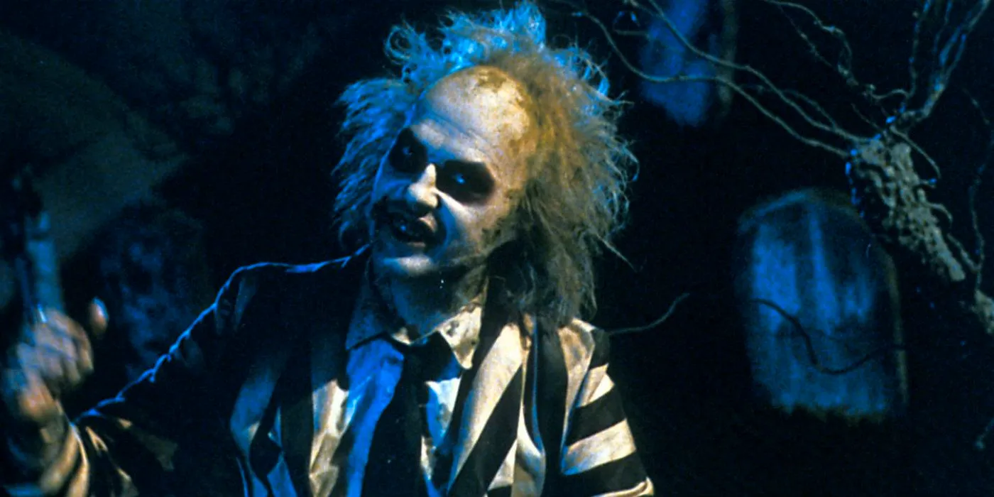 Beetlejuice standing and grinning in a dark room with his striped suit on. Image