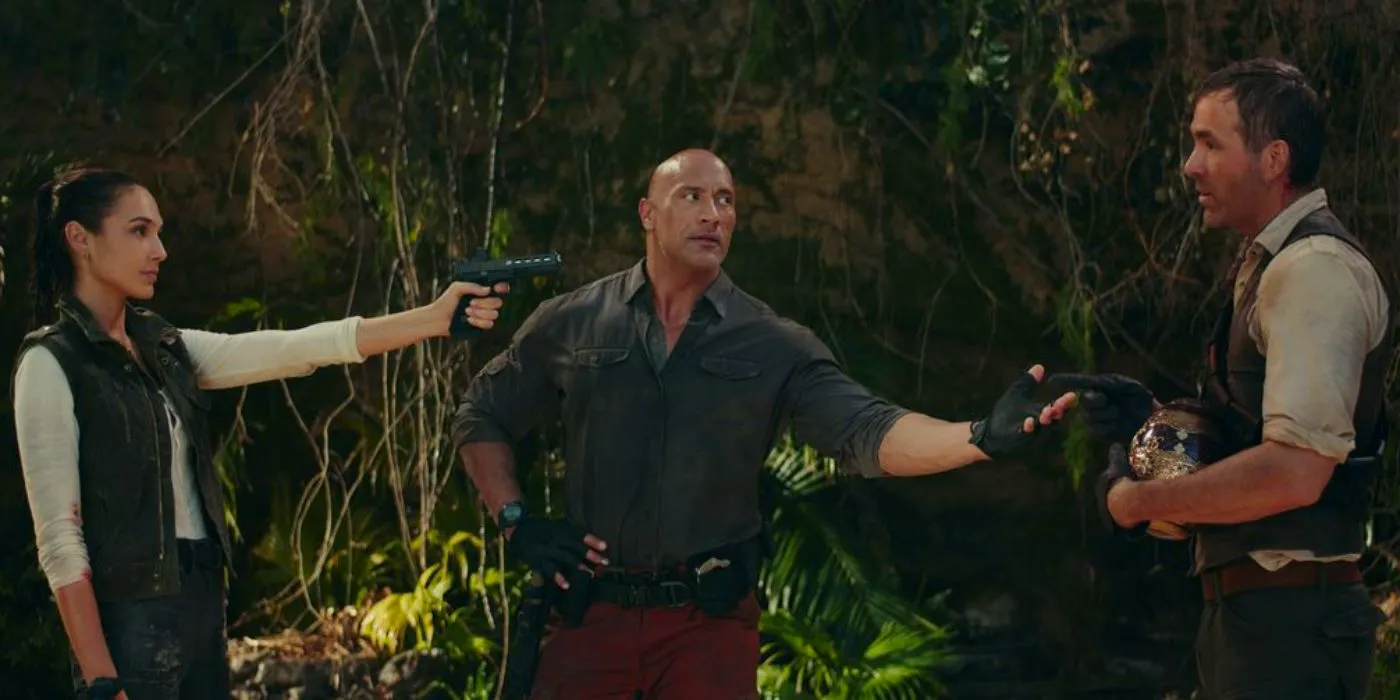 Booth (Ryan Reynolds), Hartley (The Rock), and Black (Gal Gadot) pointing guns at one another in a jungle in Red Notice Image