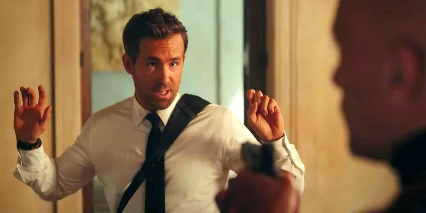 Booth (Ryan Reynolds) with his hands up at gunpoint in Red Notice Image