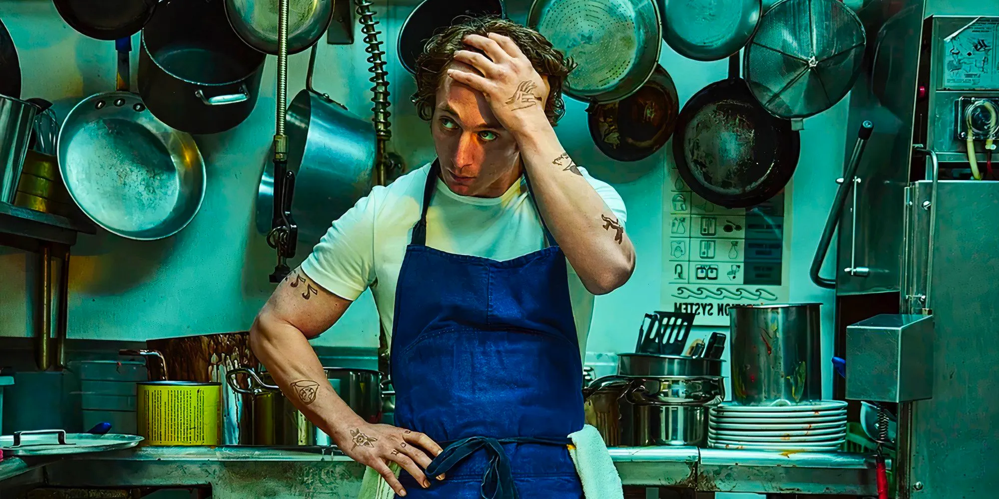 Carmen Wearing A White Tee and Blue Apron with One Hand On His Head and One On His Hip, Looking Off To Side Image