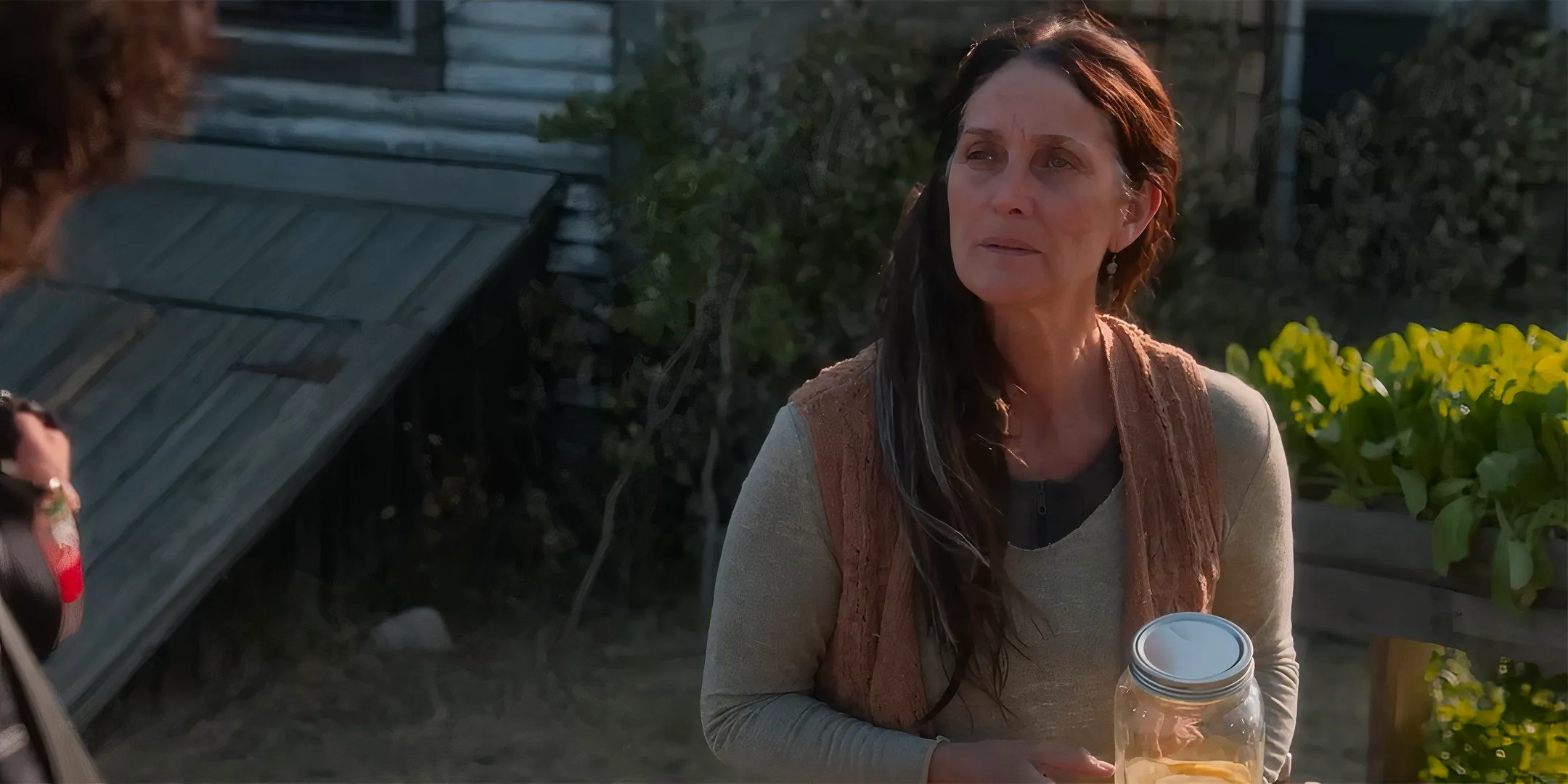 Carrie-Anne Moss as Mae looking stoically at someone while holding a jar of lemonade in Die Alone Image