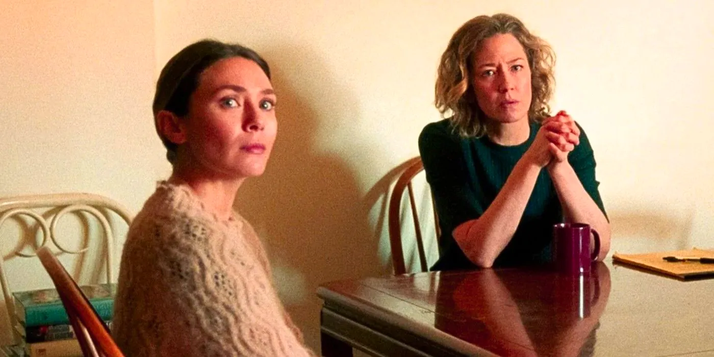 Carrie Coon and Elizabeth Olsen look at something off camera while sitting at the kitchen table in His Three Daughters Image