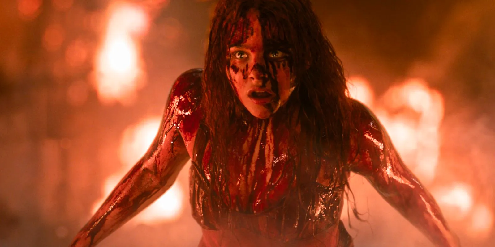 Carrie is covered in blood with flames in the background in Carrie. Image