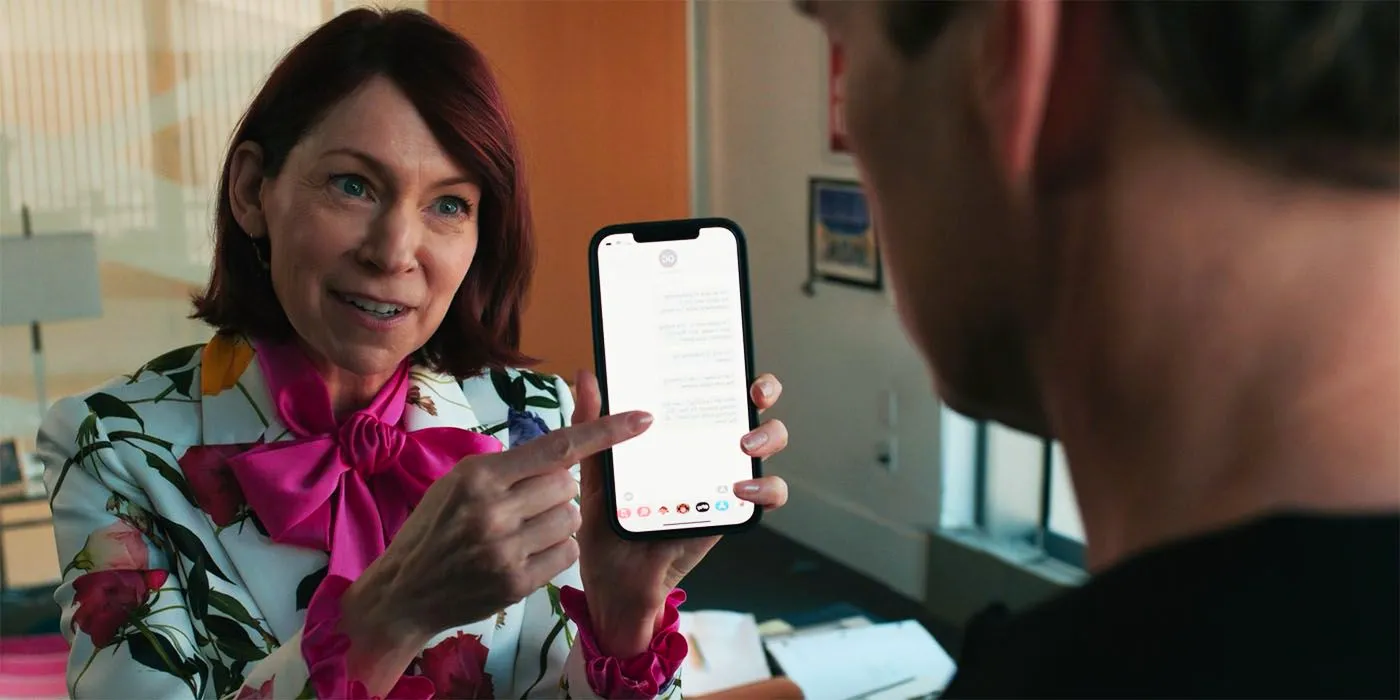 Carrie Preston smiling and pointing at a phone as Elsbeth in Elsbeth season 1, episode 1 Image