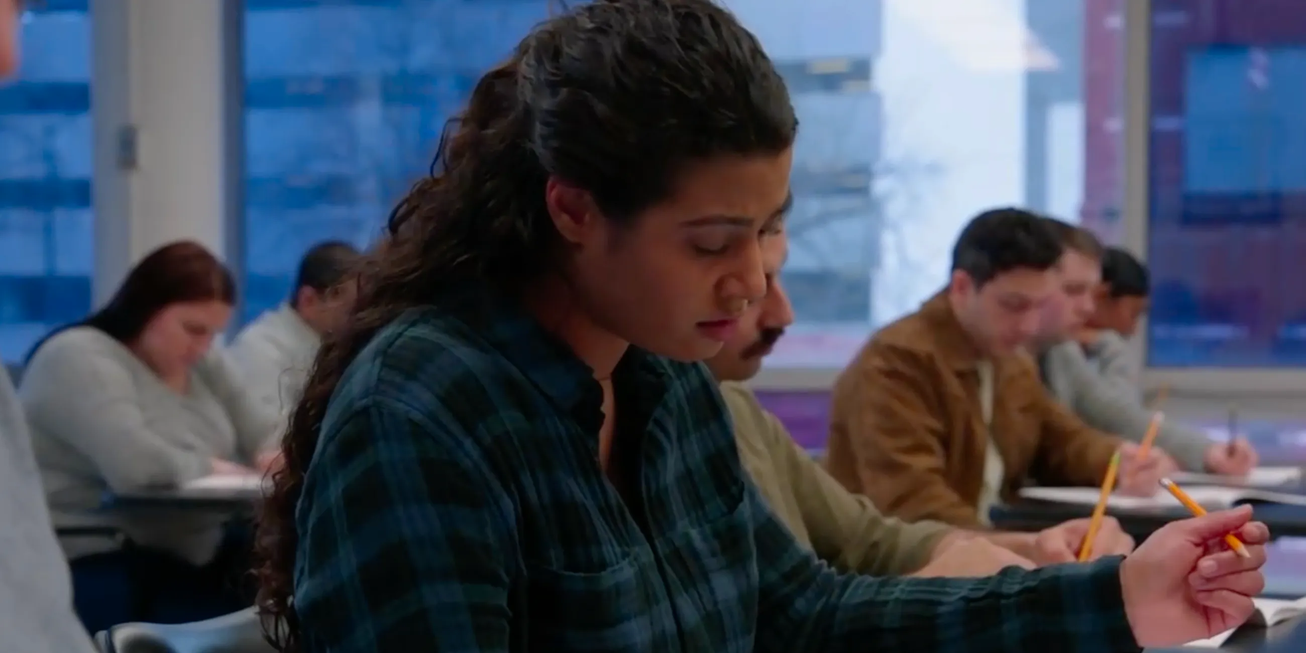 Chicago Fire Kylie sitting at a desk with a pencil and paper surrounded by other students taking the firefighter exam Image