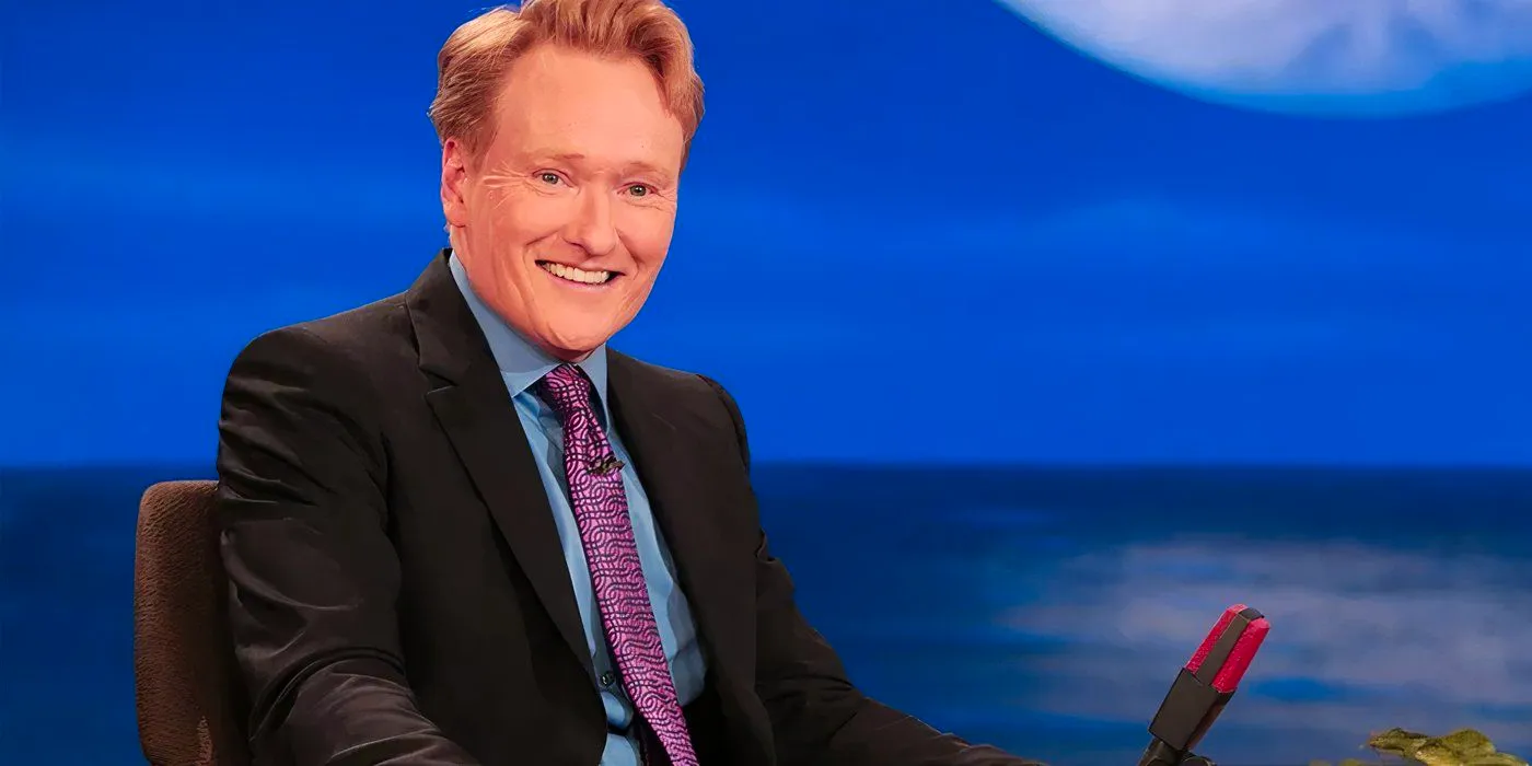 Conan O'Brien smiling behind a desk as he hosts a late-night talk show Image