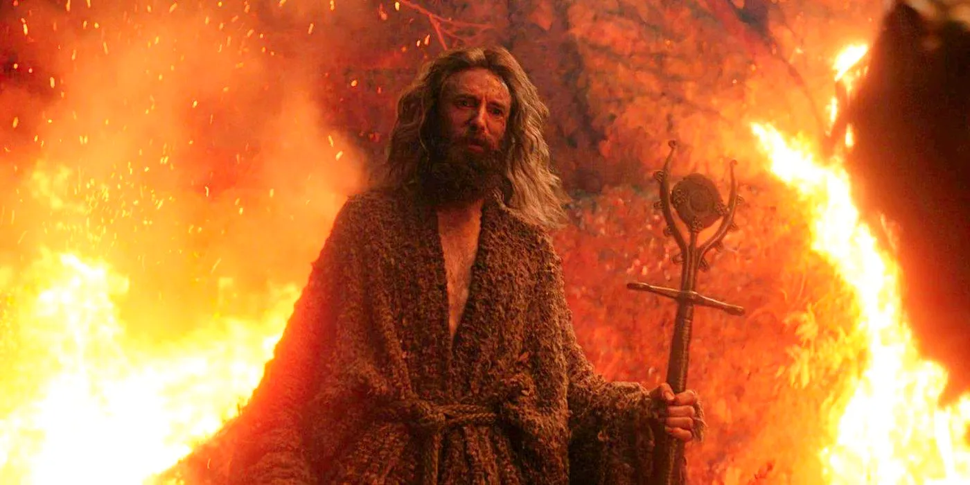 Daniel Weyman as the Stranger holding a staff and standing in front of fire in The Rings of Power. Image