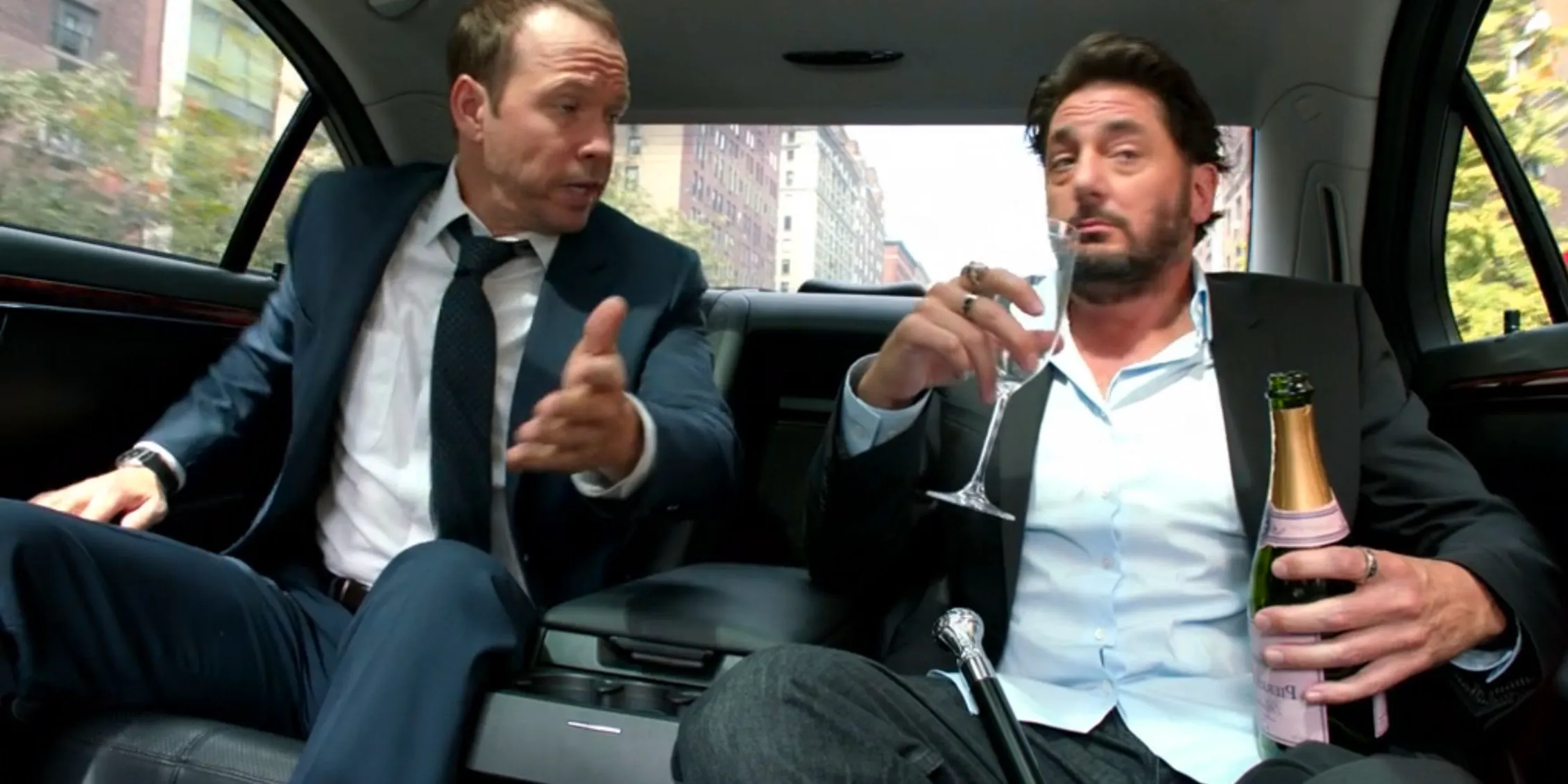 Danny in the back seat of a limo with a man who is drinking alcohol in Blue Bloods Image