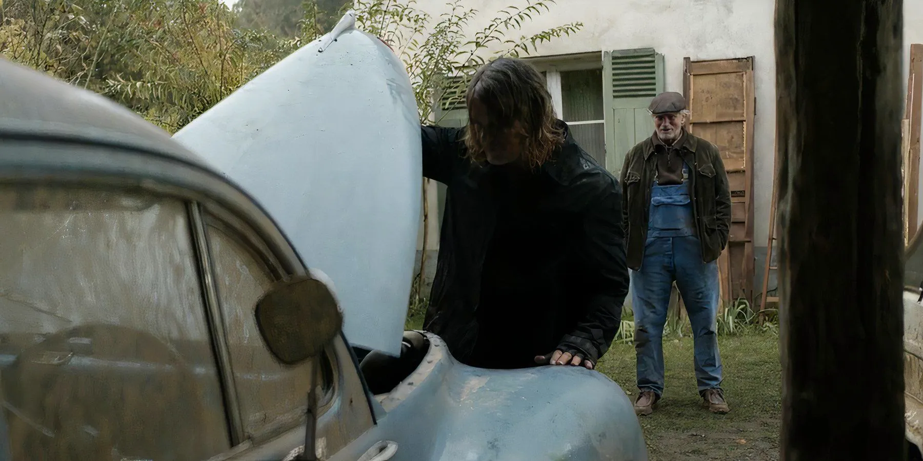 Daryl (Norman Reedus) checking the engine of a car while an older man stands behind him in The Walking Dead: Daryl Dixon Image