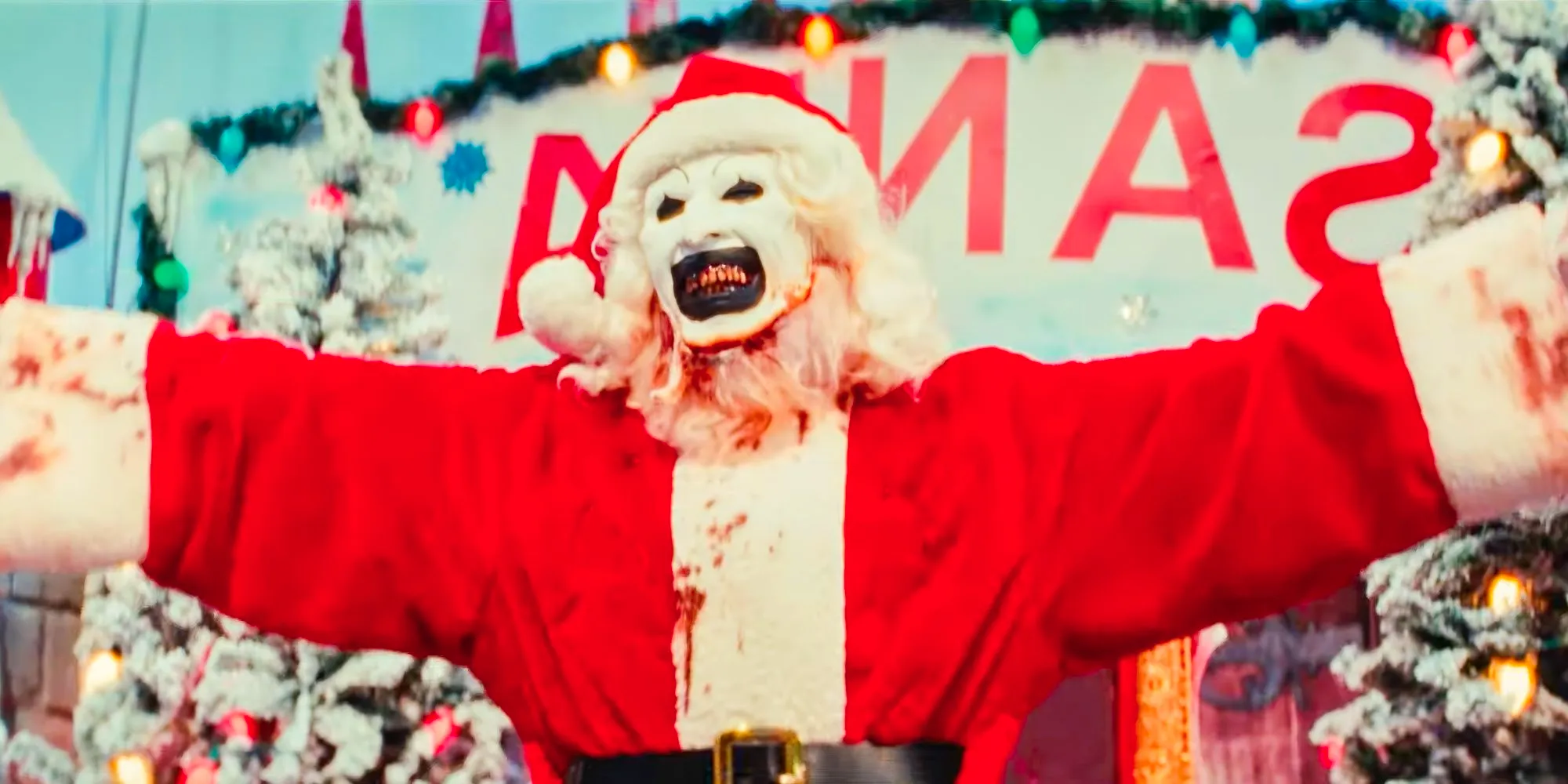 David Howard Thornton as Art The Clown dressed as santa lifting up his arms and smiling in Terrifier 3 Image