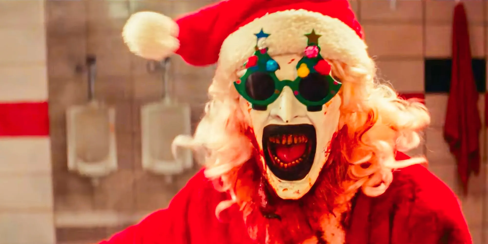 David Howard Thornton as Art The Clown in close up screaming dressed as santa with christmas tree glasses in Terrifier 3 Image