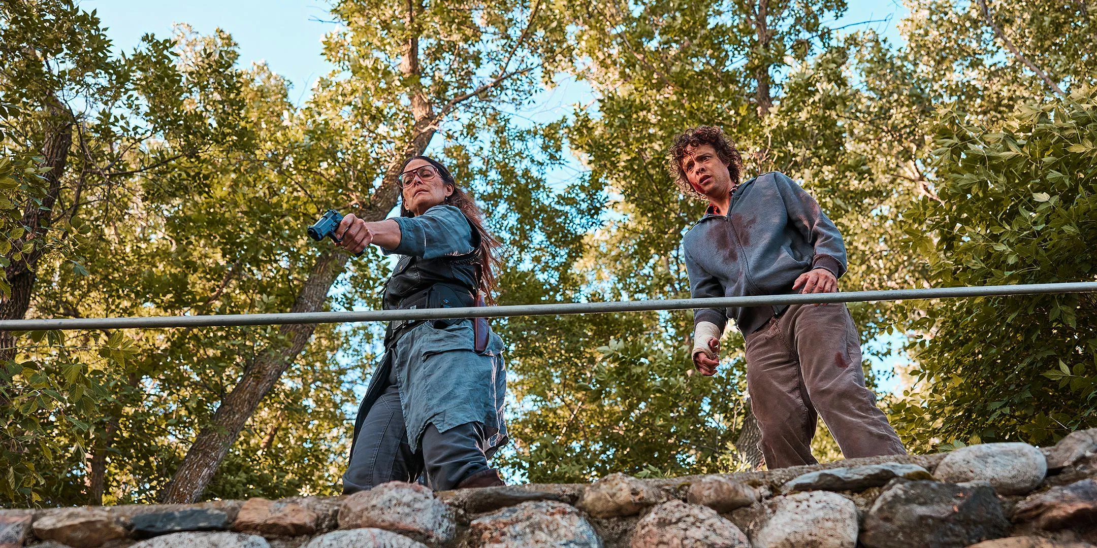 Douglas Smith's Ethan looking scared standing next to Carrie-Anne Moss' Mae aiming a gun in Die Alone Image