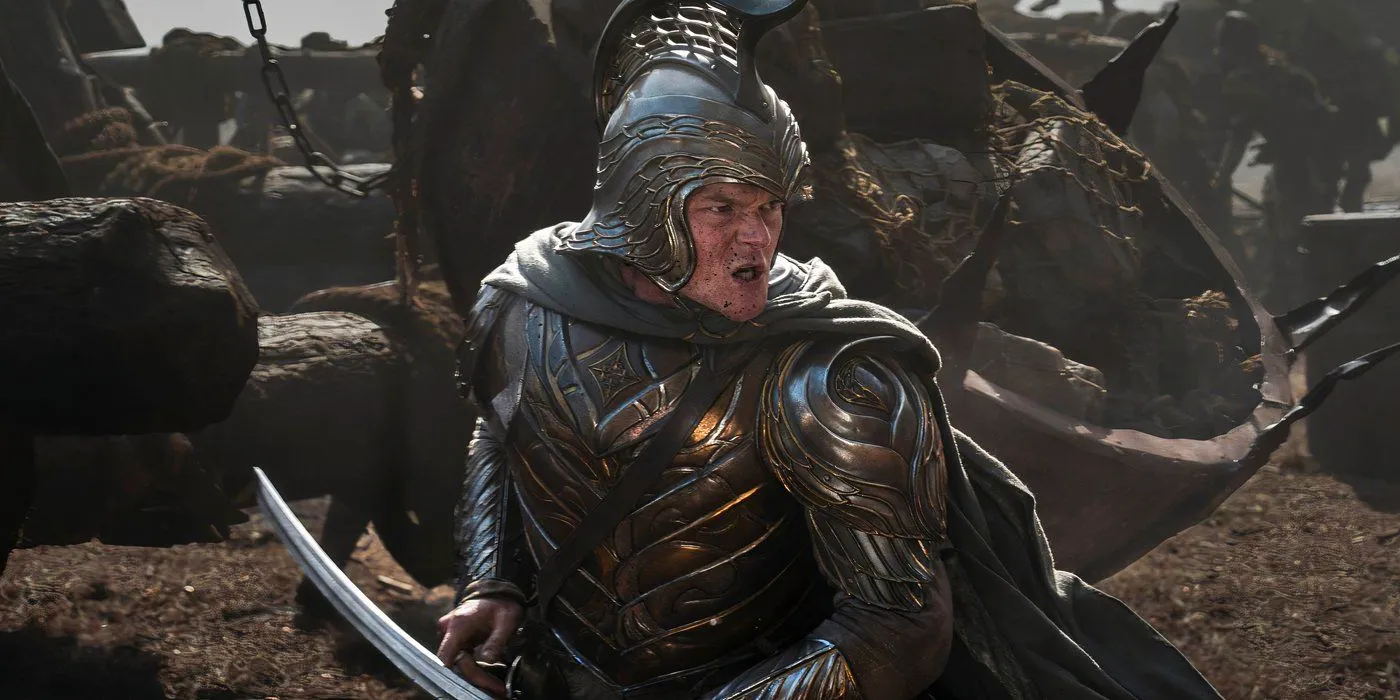 Elrond clad in armor standing in the middle of a battle with mud on his face and a sword in his hand in Rings of Power season 2 Image