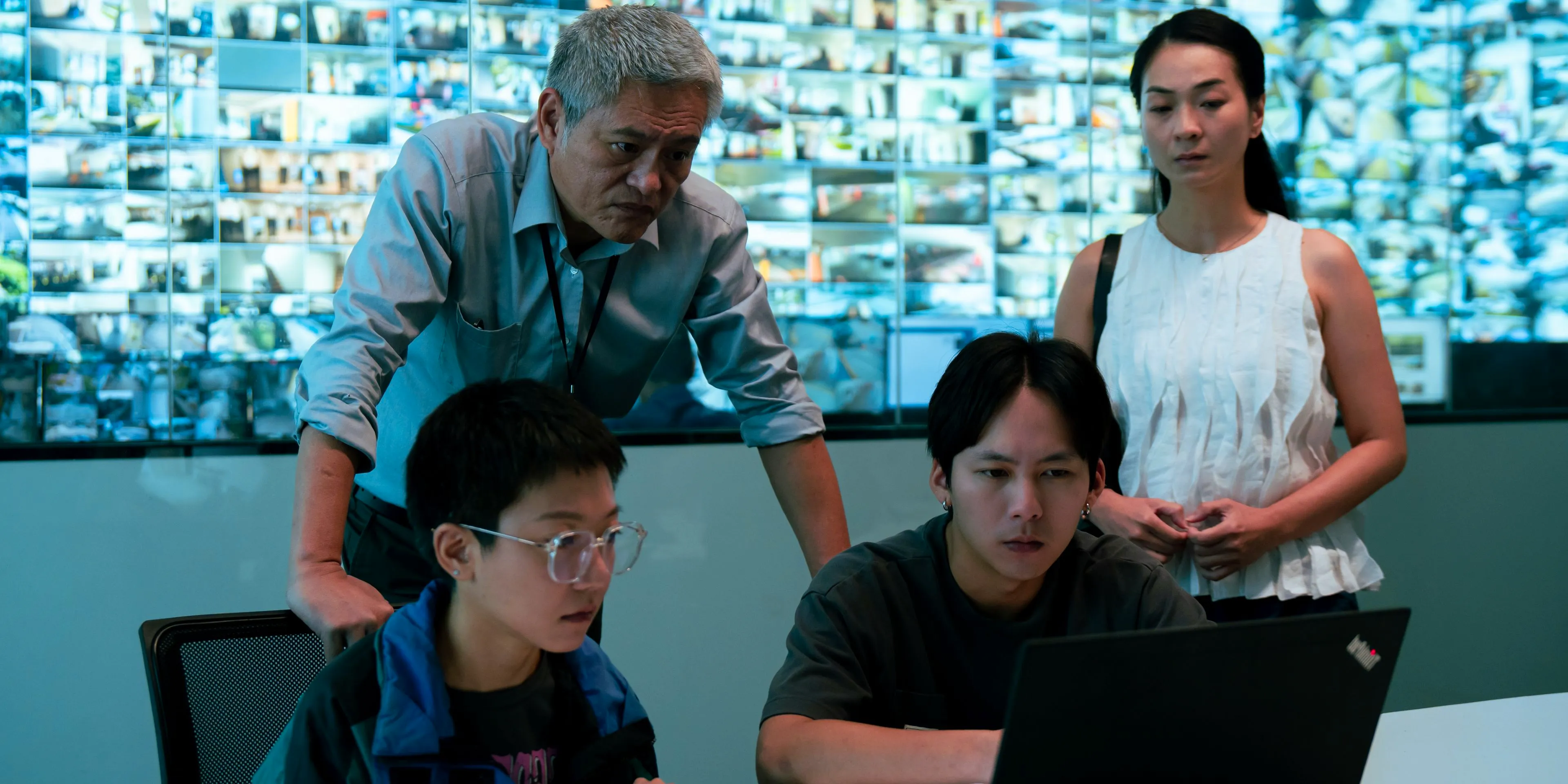 Four principal characters gathered around a laptop to watch security footage in Stranger Eyes Image