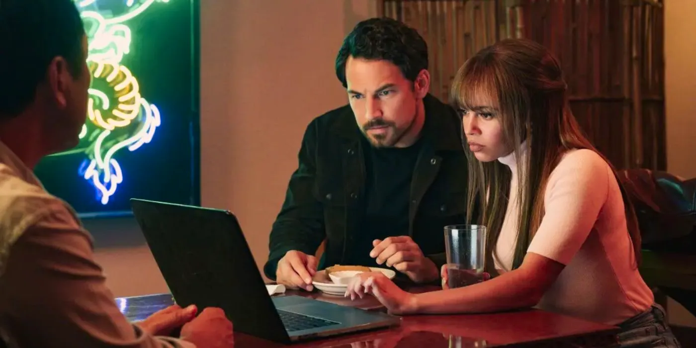 Giacomo Gianniotti as Cole Ellis and Vanessa Morgan as Max Mitchell working on a laptop together in Wild Cards. Image