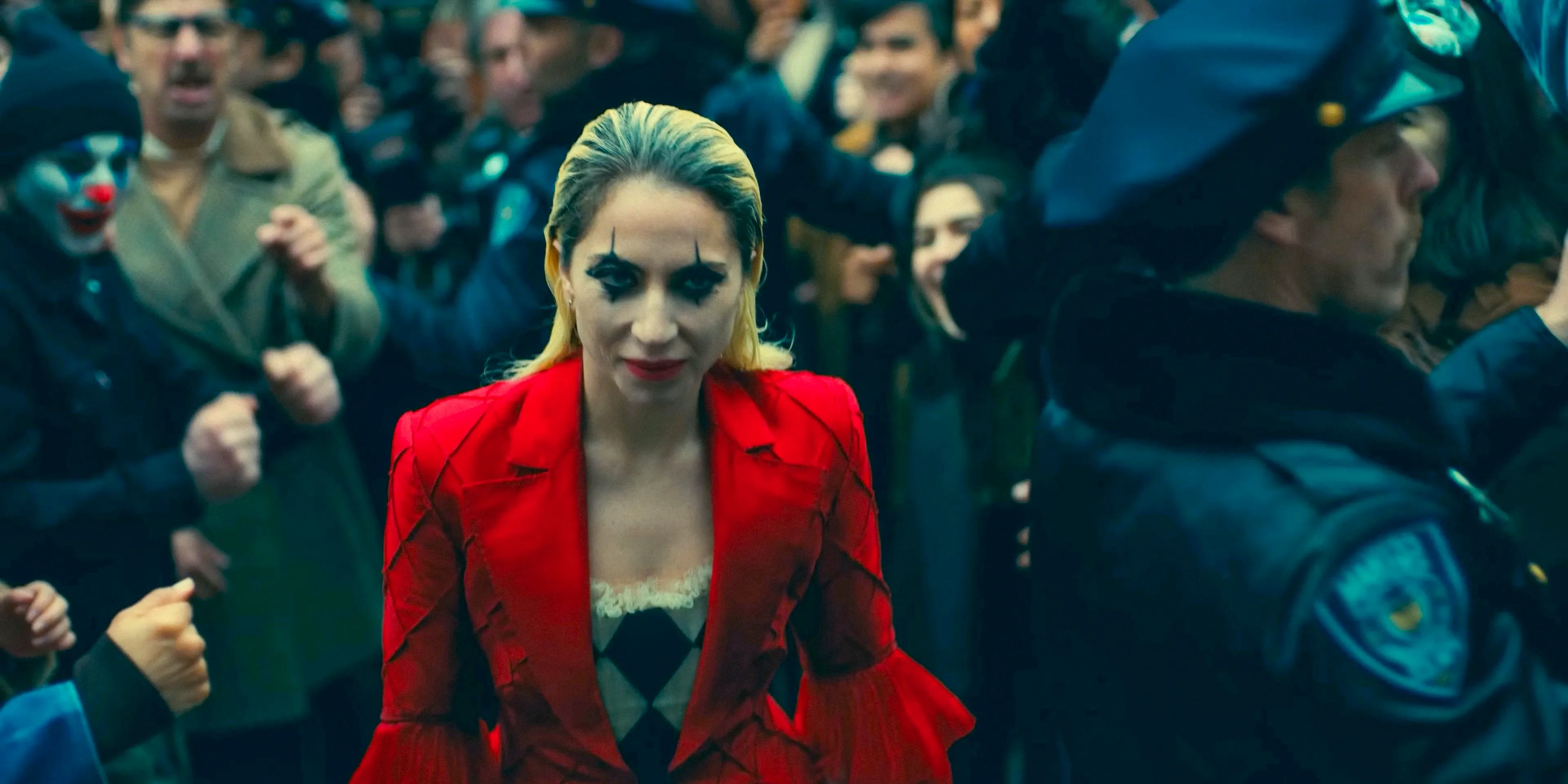 Harley Quinn (Lady Gaga), in jester makeup, smiles as she walks among fans in Joker: Folie à Deux Image