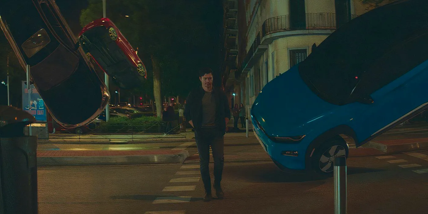 Henry Golding walks through a street with flipping cars in Daniela Forever Image