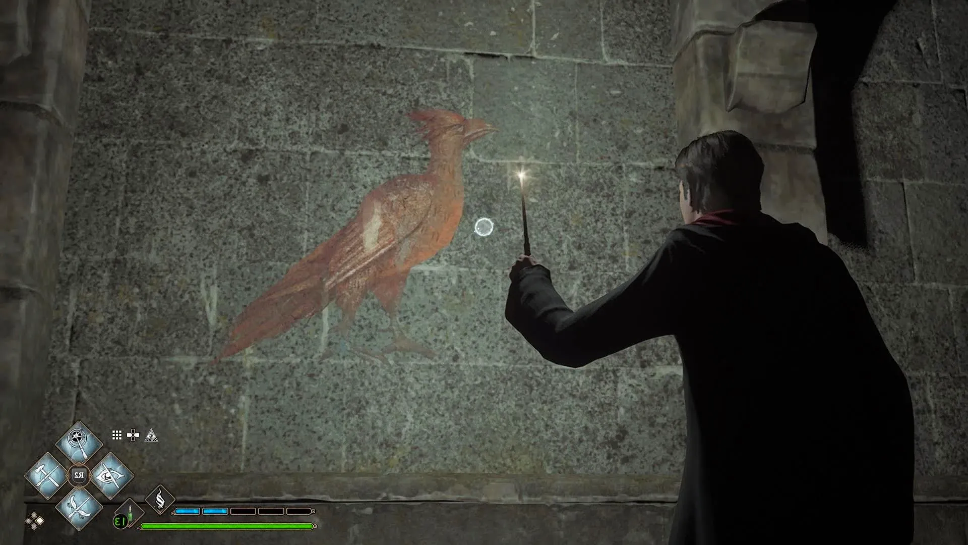 Image of a character standing in front of a wall in the Hogwarts Castle with his wand lit up looking at the Phoenix that is painted on the wall where Dumbledores office used to be in older games.  Image