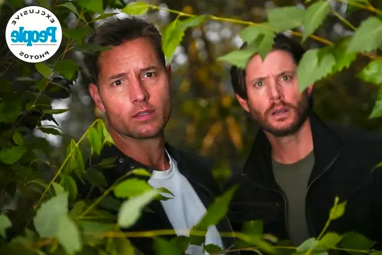 Jensen Ackles as Russell and Justin Hartley as Colt stand among trees and look beyond branches in Tracker season 2 Image