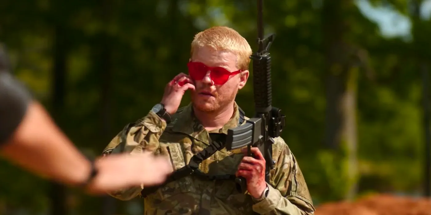 Jesse Plemons wearing red shades and holding his gun while scratching his cheek in Civil War Image