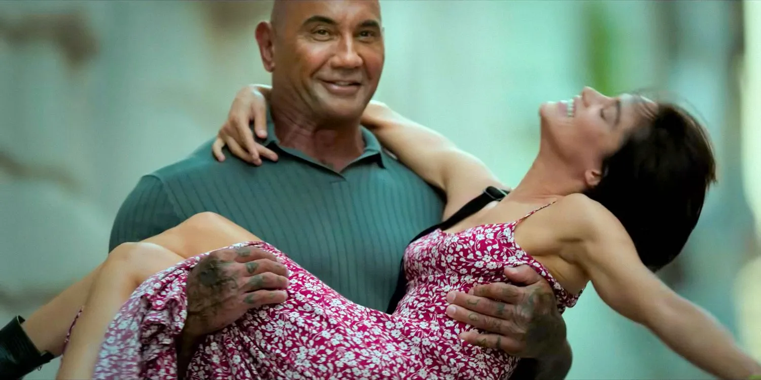 Joe Flood (Dave Bautista) smiling while carrying Maize (Sofia Boutella) in his arms in The Killer's Game (2024) Image