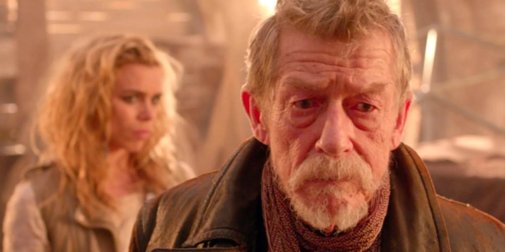 John Hurt as the War Doctor looking serious with Billie Piper as Bad Wolf over his shoulder Image