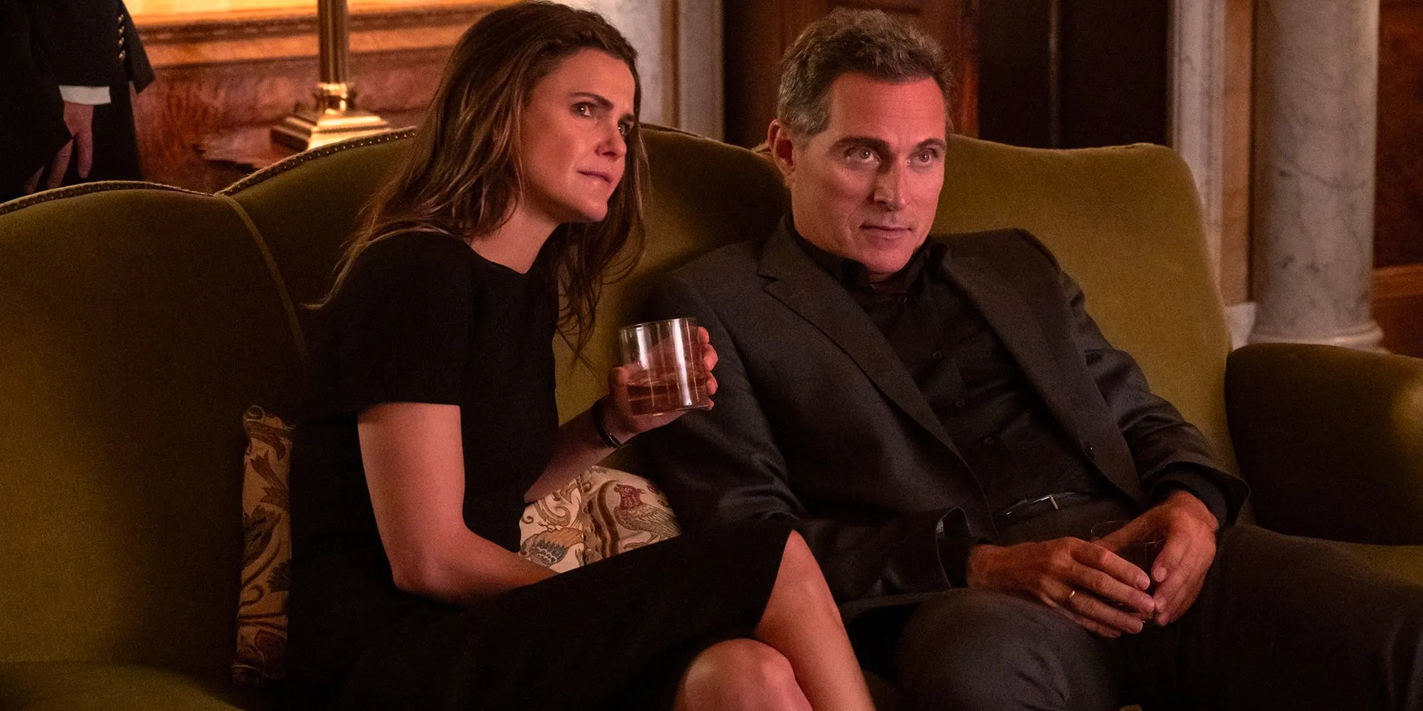 Kate (Keri Russell) and Hal (Rufus Sewell) sitting on a couch listening to someone talk in The Diplomat Image