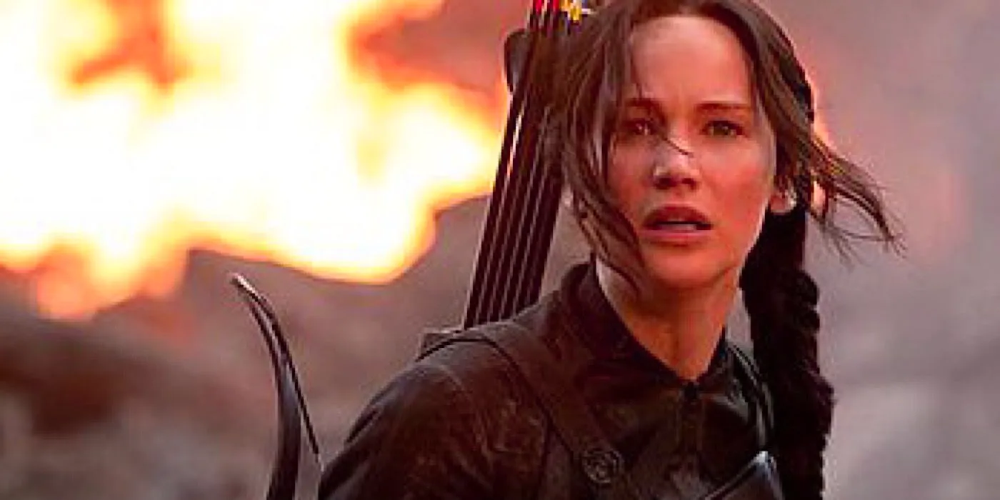 Katniss looks into the distance as fire rages behind her in The Hunger Games. Image