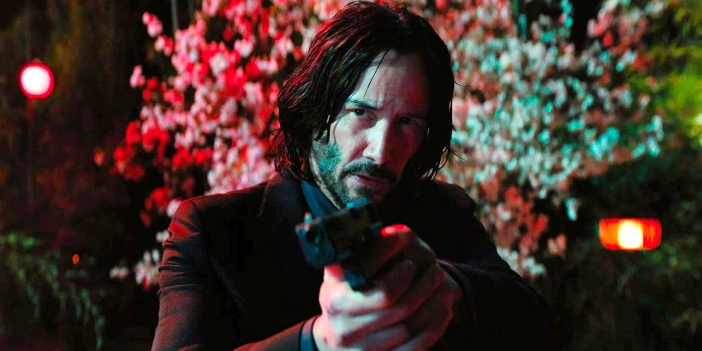 Keanu Reeves as John Wick aiming a gun with trees in the background - John Wick: Chapter 4 Image