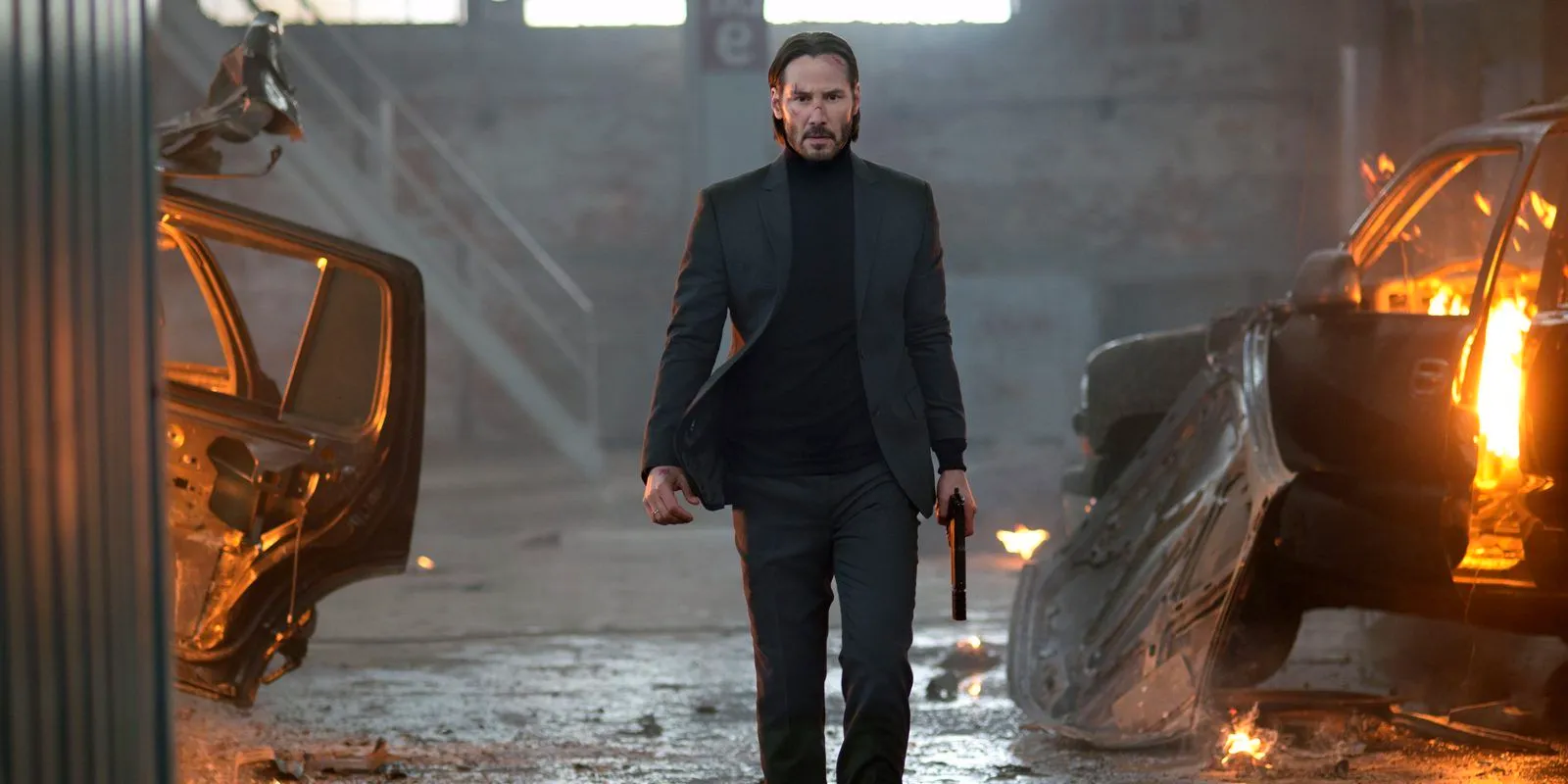 Keanu Reeves holding a pistol in a warehouse with destroyed cars in John Wick (2014) Image