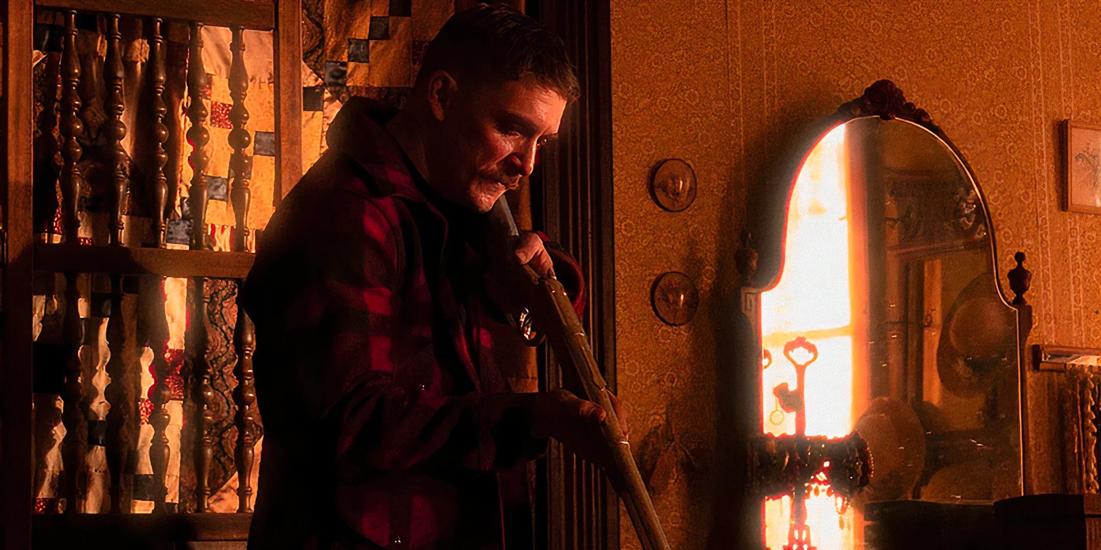 Kyle Gallner as The Demon aiming his rifle towards the ground in a bedroom in Strange Darling Image