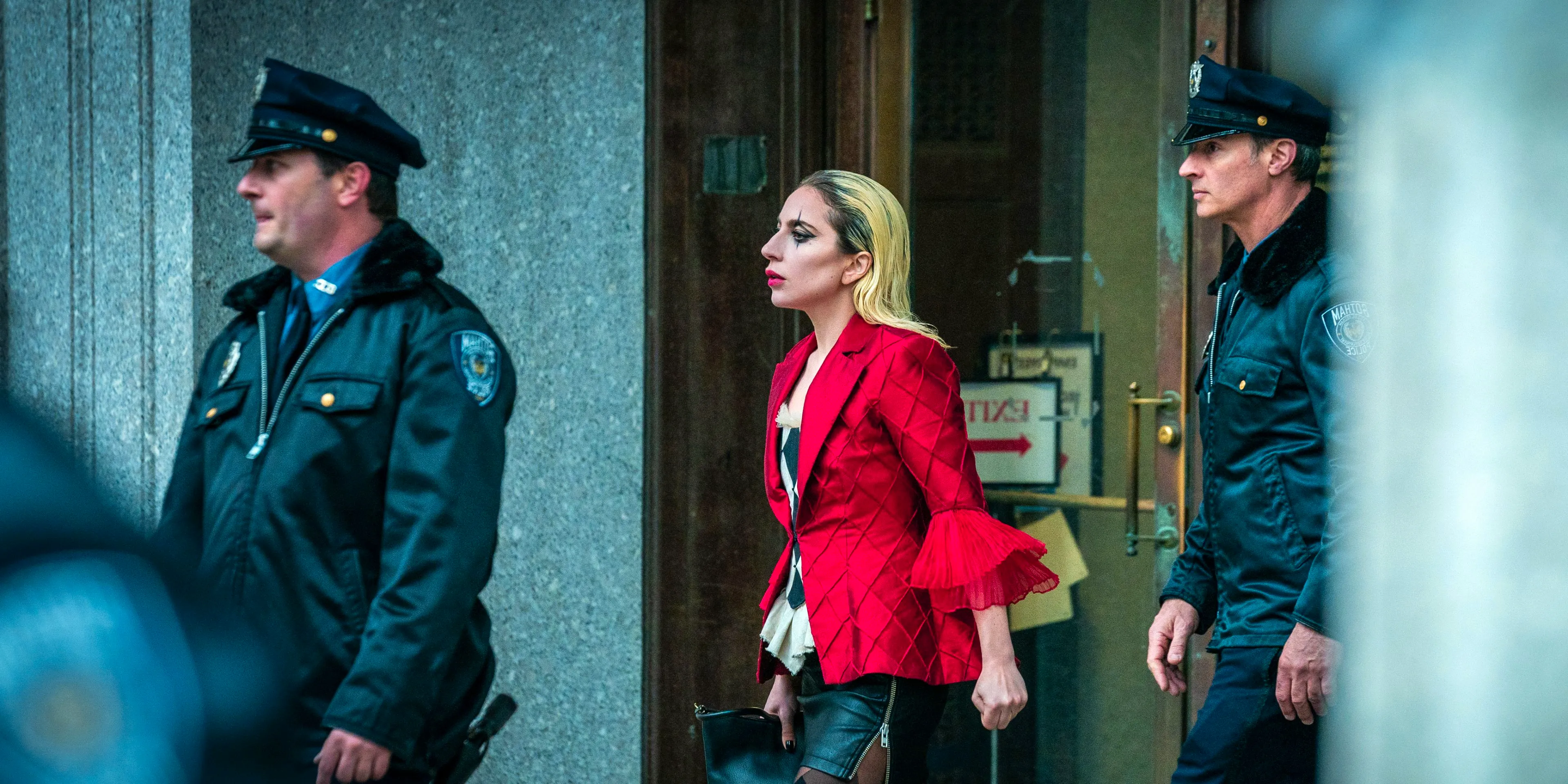 Lady Gaga as Harley Quinn in makeup and flanked by policemen in Joker Folie a Deux Image