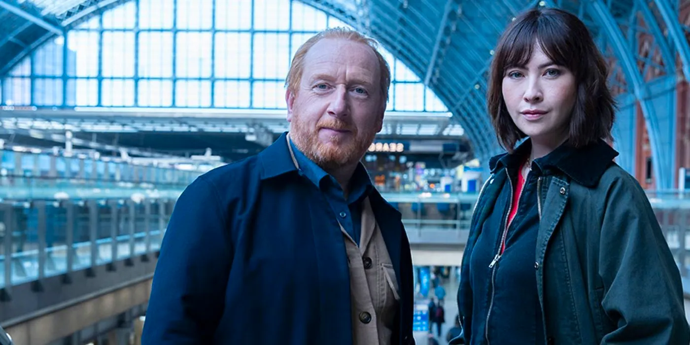 Layla (Vanessa Emme) and Max (Adrian Scarborough) standing together in a train station in The Chelsea Detective. Image