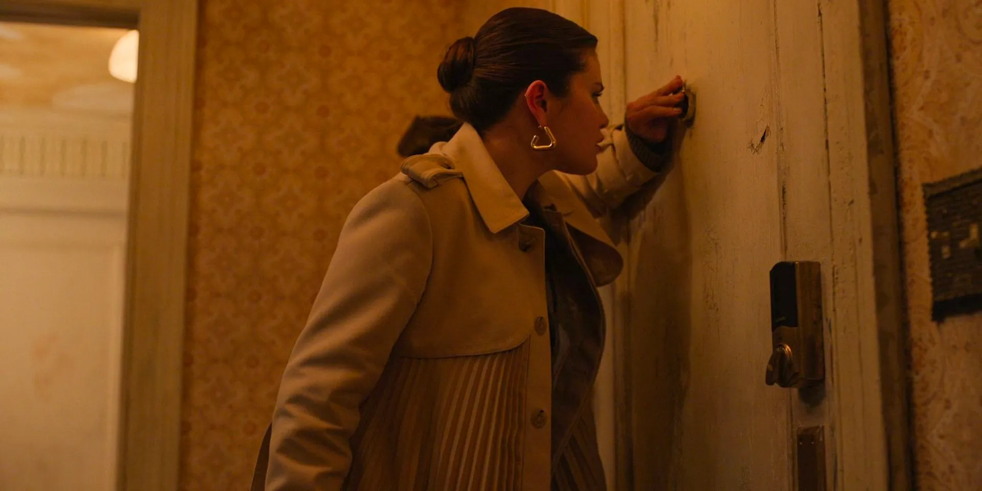 Mabel (Selena Gomez) peeks through the peephole to see who is knocking on Dudenoff's door in Only Murders in the Building Season 4 Episode 2 Image