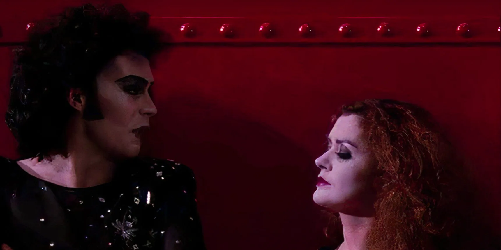 Magenta and Frank talking against a red wall in Rocky Horror Picture Show Image