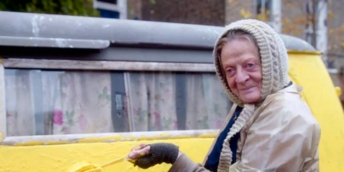 Maggie Smith as Miss Shepherd smiling outside a yellow van in The Lady in the Van Image