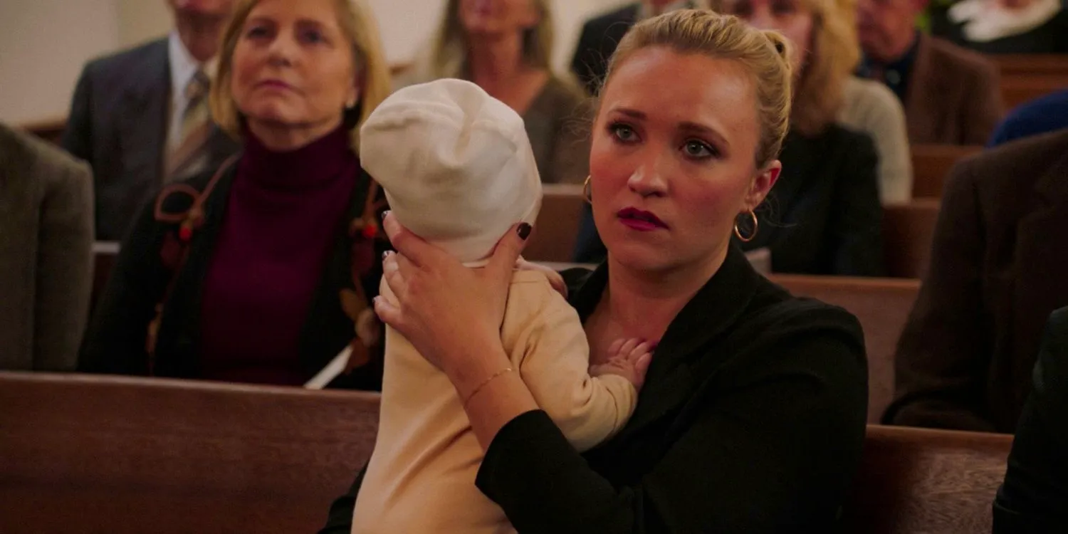 Mandy McAllister (Emily Osment) had a serious expression while holding her baby at George's funeral in Young Sheldon season 7 episode 13 Image