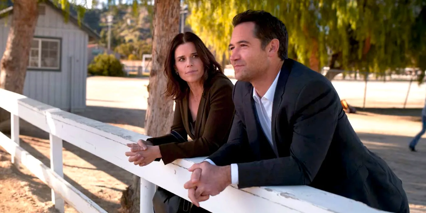 Manuel Garcia-Rulfo and Neve Campbell Leaning Against a Fence in The Lincoln Lawyer Season 2 Image