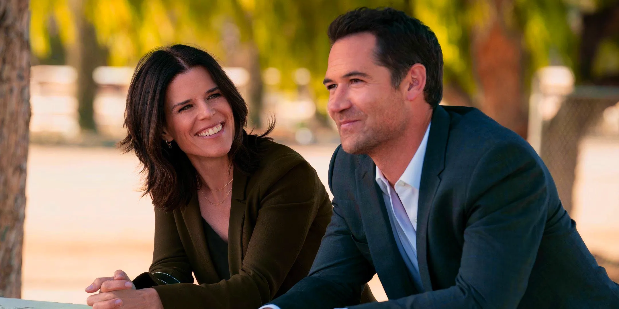 Manuel Garcia-Rulfo as Mickey and Neve Campbell as Maggie smiling in The Lincoln Lawyer Image