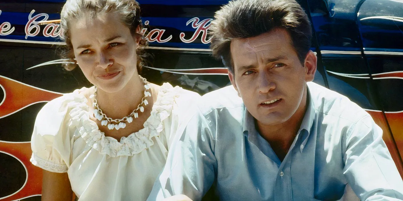 Martin Sheen and Michelle Phillips are crouching with their backs against a car.  Image