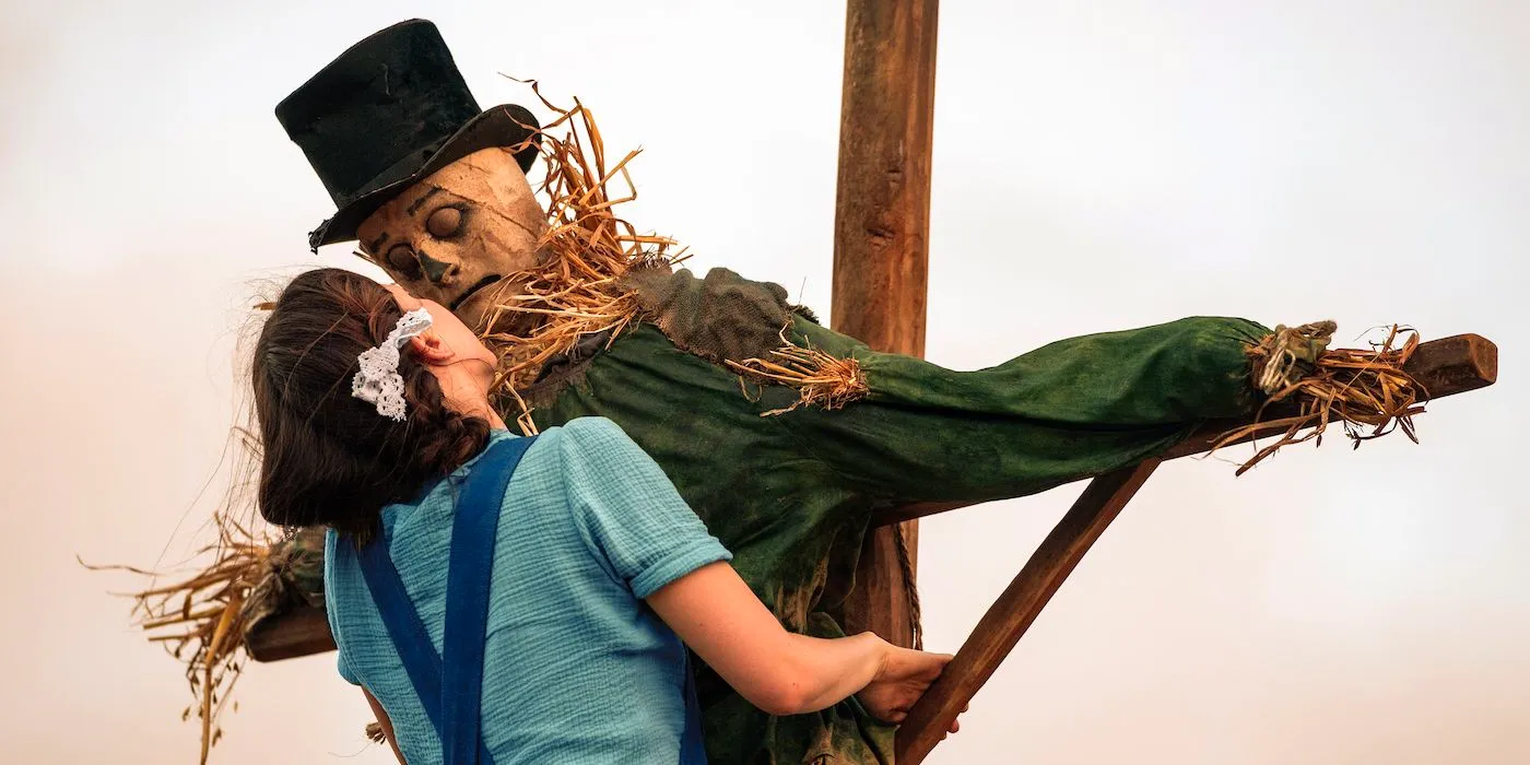 Mia Goth as Pearl climbing up a scarecrow in Pearl Image