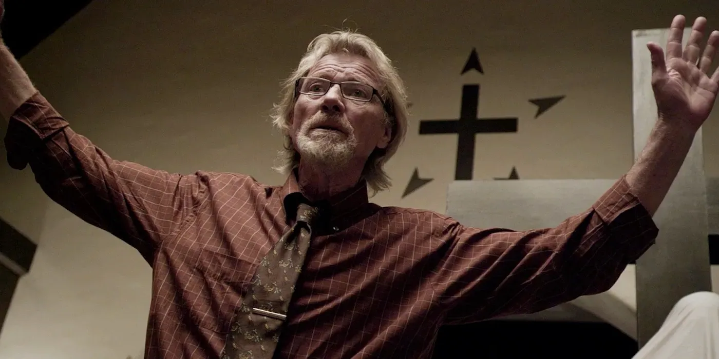 Michael Parks stands in a church with his arms outstretched in Red State Image