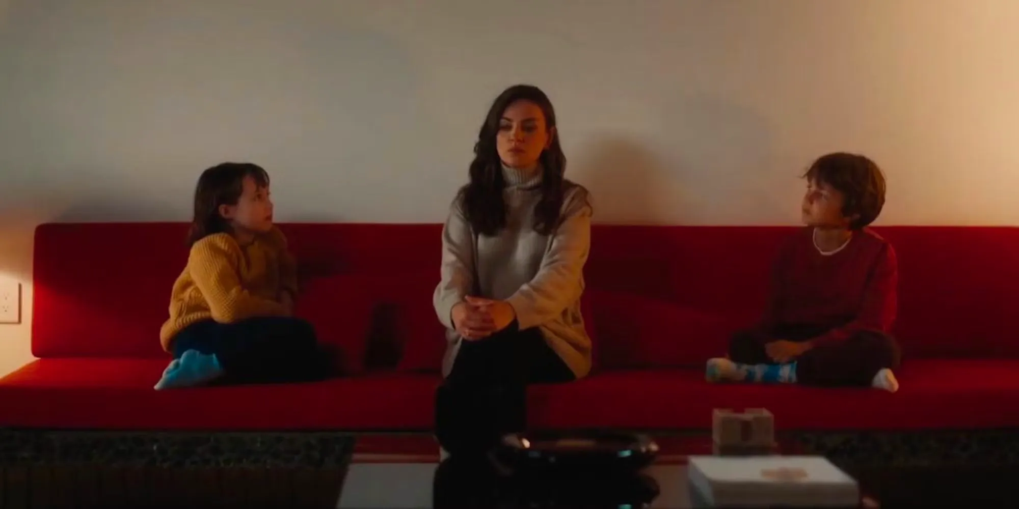 Mila Kunis sitting with the kids on red couch Image