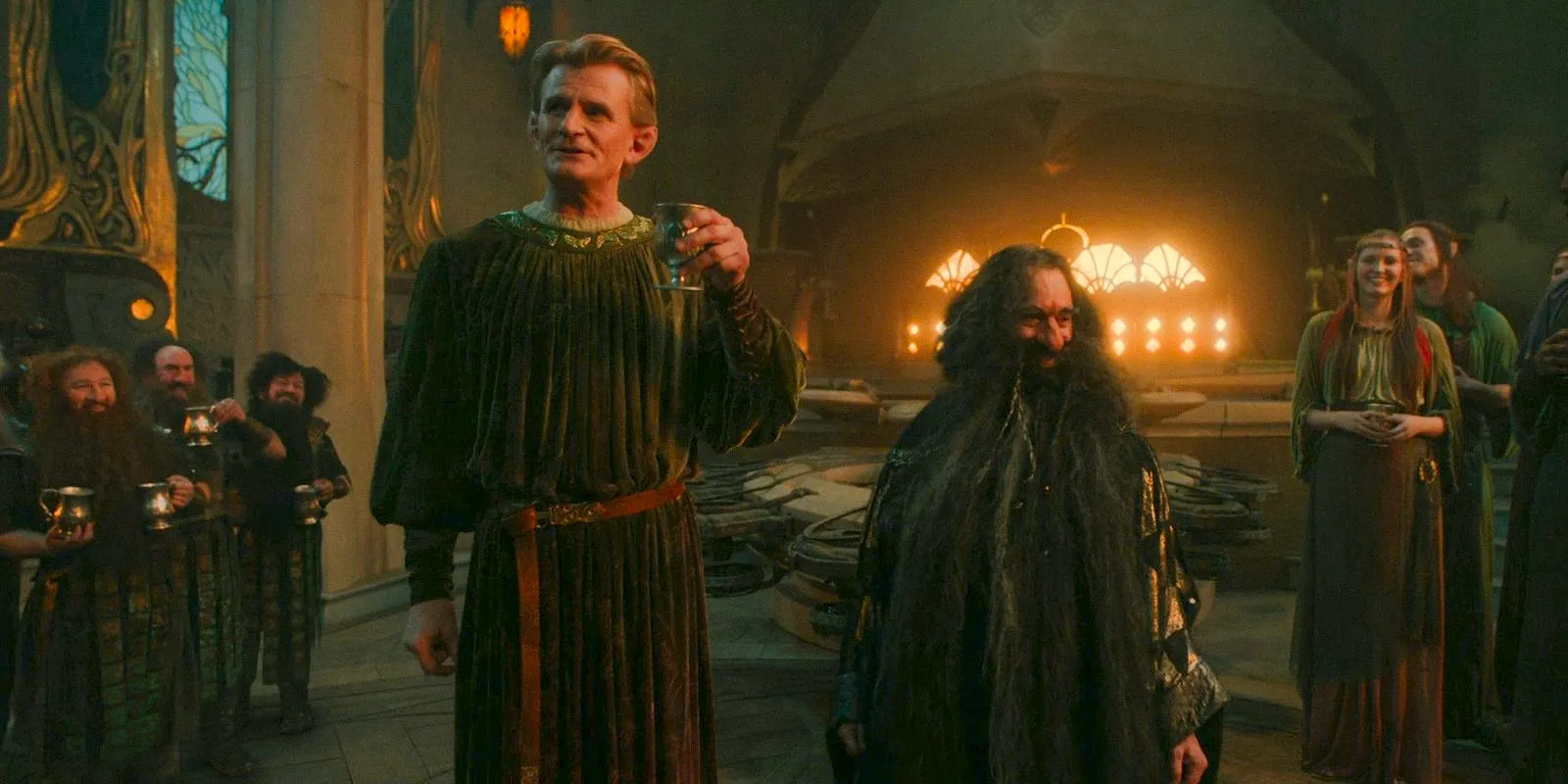 Narvi (Kevin Eldon) and Celebrimbor (Charles Edwards) toasting to the new alliance between dwarves and elves in The Lord of the Rings: The Rings of Power Season 2 Episode 5 Image