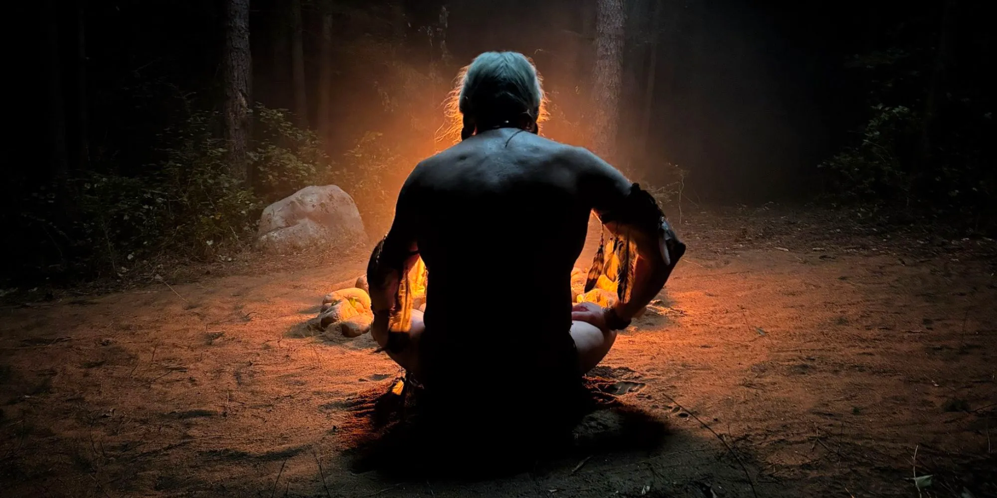 Peacemaker season 2's mystery character sitting in front of a campfire Image